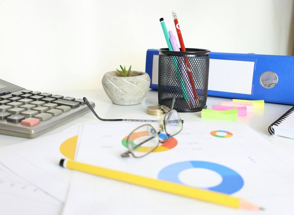 A desk with a calculator, reports, a blue file and stationery